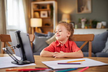 A young child smiles while sitting at a table covered with paper and colored pencils. The family atmosphere is warm, highlighting moments of joy and creativity in a comfortable living room.