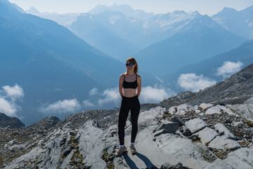 A woman standing on a rocky mountain top with mountains in the distance.