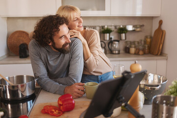 In a cozy kitchen, a couple shares a joyful moment while preparing a meal. Fresh vegetables are on the counter, and smiles brighten the space as they interact.