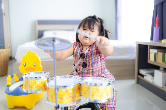 A cute little Asian girl is happily playing a toy drum,Little toddler drummer girl playing and hitting the drum set at home.Asian girl playing and singing happy moment in music lesson time.