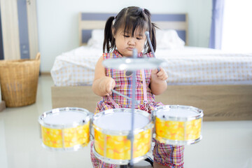 A cute little Asian girl is happily playing a toy drum,Little toddler drummer girl playing and...