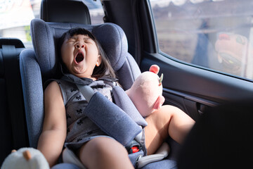 A cute little Asian girl is sitting sleepily on the back seat of a car,Yawn,A little girl is...