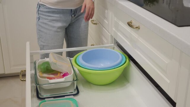 Woman Tidy Puts Plastic Lid on Bowl in Drawer and Gently Closes Cabinet.