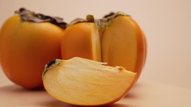 A juicy persimmon slice lies in front of whole fruits as the arrangement slowly rotates. The video focuses on rich orange color and smooth texture.