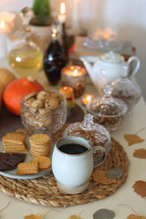 Lit candles, cookies, chocolate, nuts, tea, wine, pumpkins, books, reading glasses and autumn leaves on the table. Autumnal hygge at home. Selective focus.
