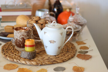 Lit candles, cookies, chocolate, nuts, tea, wine, pumpkins, books, reading glasses and autumn leaves on the table. Autumnal hygge at home. Selective focus.