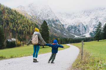 Family hiking together in nature. Woman with son running on road with mountain view in autumn. Mother and child together outdoors. Adventure travel with kids in nature.