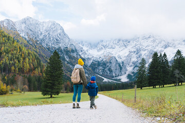 Family hiking together in nature. Woman with son running on road with mountain view in autumn. Mother and child together outdoors. Adventure travel with kids in nature.