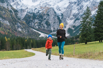 Family hiking together in nature. Woman with son running on road with mountain view in autumn. Mother and child together outdoors. Adventure travel with kids in nature.