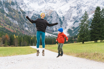 Family hiking together in nature. Woman with son running on road with mountain view in autumn. Mother and child together outdoors. Adventure travel with kids in nature.