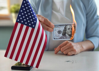 Person holding a burning hundred dollar bill next to a small American flag concept
