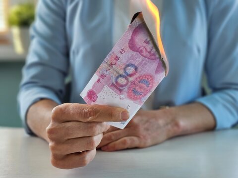A person is holding a burning Chinese yuan note, showing a worried expression