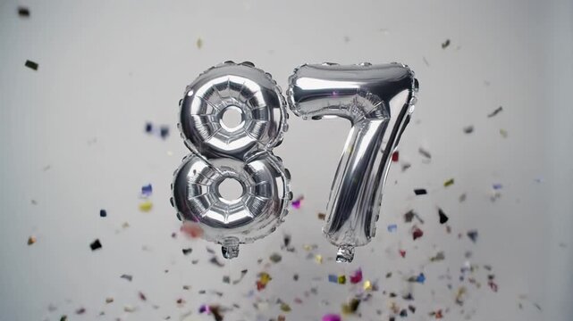Silver balloon number 87 for birthday or anniversary party. White background with falling confetti