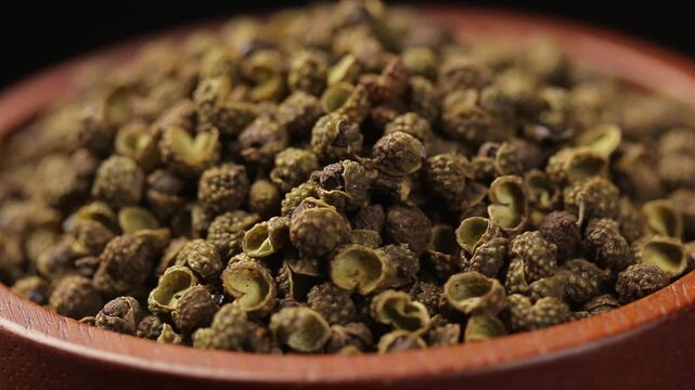 Pile of dried green szechuan peppercorns or chinese prickly ash in a brown wooden bowl rotating. Close-up shot