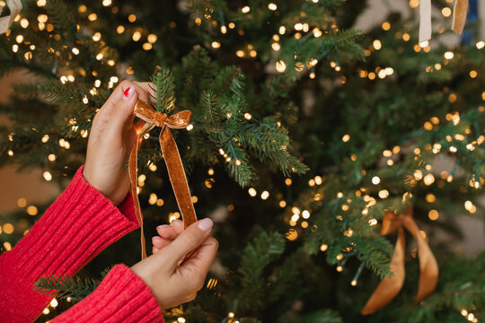 Close-up of a woman decorating an illuminated Christmas tree with a velvet ribbon ornament - Powered by Adobe