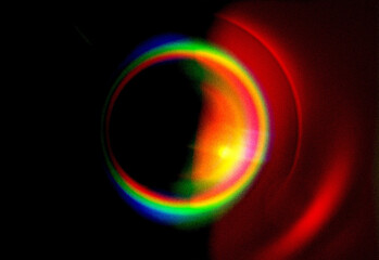 Abstract close up of a circular rainbow light ring against a dark background, created by lens flare and prism reflections, capturing vibrant spectrum and energy