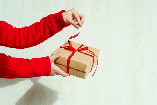 Close-up of a woman's outstretched hands holding and opening a gift box tied with a red ribbon