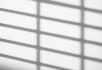 Abstract black and white photograph of window blinds casting diagonal shadows across a smooth light surface, creating a minimal pattern with soft gradients and subtle texture