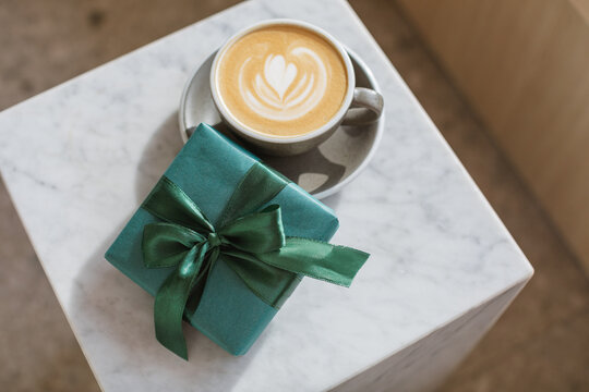 Close-up overhead view of a cappuccino coffee and a wrapped gift on a side table