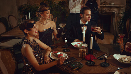 Smiling retro women and men enjoying elegant dinner party in vintage restaurant. Concept of event marketing, themed retro evenings, premium hospitality visuals, social nightlife content.