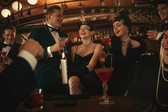 Retro bar group laughing and raising cocktails in joyful glamorous nightlife moment. Concept of social media nightlife visuals, bar promotions, mixology events, luxury brand storytelling.