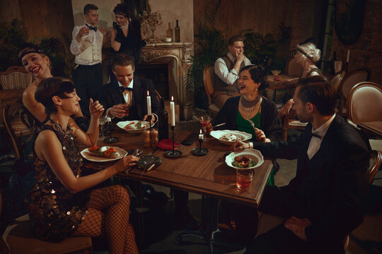 Retro dinner gathering with laughing friends enjoying elegant vintage restaurant evening. Concept of holiday event campaigns, luxury dining visuals, themed retro marketing, nightlife social content.