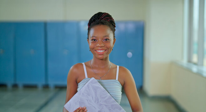 African young adult gen z beautiful lady confident student standing hold laptop look camera indoor campus happy smiling girl staring cam do casual pose slow motion enjoy day time inside college