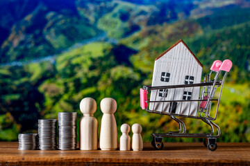 Small wooden toy house in shopping cart, stack of coins and figures of people on nature background. Concept of save money for purchase or construction of home, mortgage and real estate investment