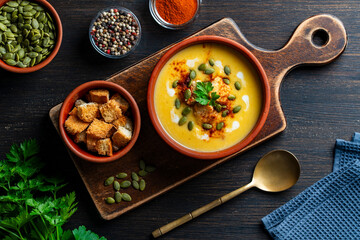 Delicious pumpkin cream soup with baked bread and pumpkin seeds in a ceramic bowl on a wooden table, closeup, top view. Healthy food concert