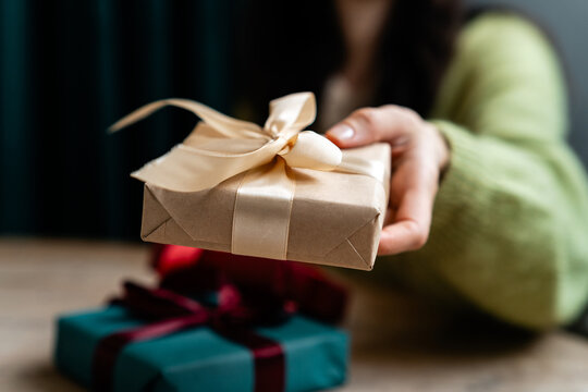 Close-up of a woman sitting at a table with wrapped Christmas gifts holding a gift box tied with a red ribbon