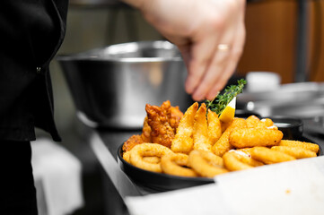 A close-up shot of a restaurant's tasty deep-fried seafood appetizer platter featuring golden calamari rings, fish bites, shrimp, lemon, and a thyme garnish.