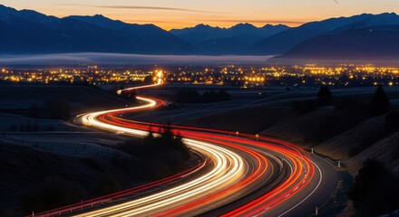 Light trail on a winding road at dusk with city lights and mountains