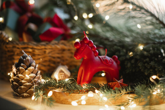 Close-up of a rocking horse candle, pinecone, fir branches and illuminated Christmas fairy lights on a table