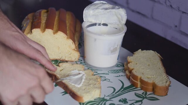 Close-up of Hand Spreading Cream Cheese on a Slice of Freshly Baked Bread