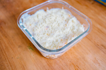 Square glass bowl of grated parmesan cheese on a wooden surface.