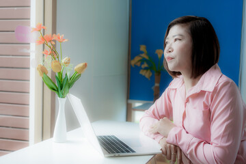 Businesswoman smiling while using laptop and talking on mobile phone at desk in office and at home or coffee shop.