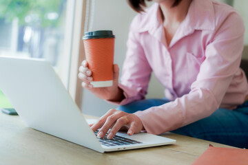 Businesswoman smiling while using laptop and talking on mobile phone at desk in office and at home or coffee shop.