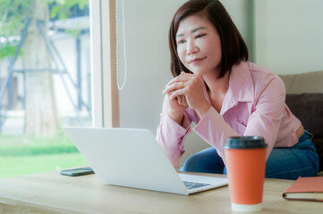 Businesswoman smiling while using laptop and talking on mobile phone at desk in office and at home or coffee shop.