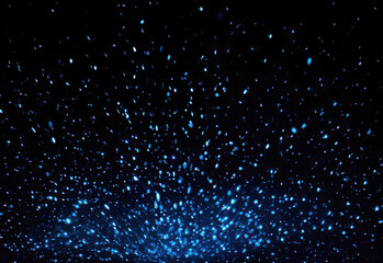An expansive field of glowing blue particles floats across a black background, forming an abstract cosmic glow with shimmering specks reminiscent of distant stars and space dust