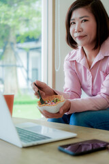 Businesswoman smiling while using laptop and talking on mobile phone at desk in office and at home or coffee shop.