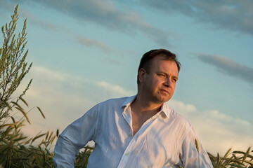 Man in white shirt standing in rye field at sunset