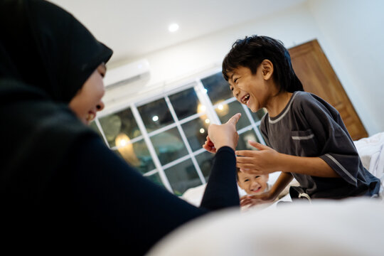 A mother and her son laugh together while the younger child watches with excitement, capturing a lively family moment at home.