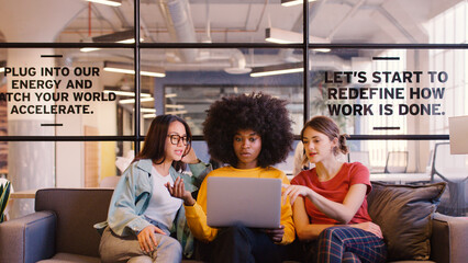 Three Young Businesswomen Working On Laptop In Informal Seating Area Of Modern Office