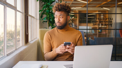 Young Businessman With Piercing At Desk Using Smart Phone In Modern Office