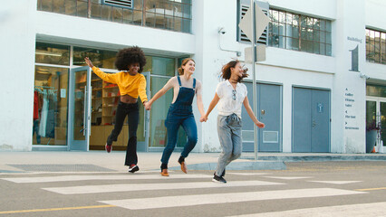 Three Young Smiling Female Friends Outdoors Holding Hands On Crosswalk In City