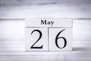 A wooden calendar block displays the date May 26 on a light wooden surface, symbolizing the passage...