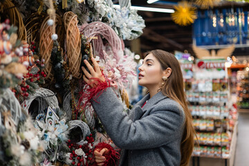 Young woman selecting Christmas wreaths at an outdoor holiday market with various decorative ornaments on display.