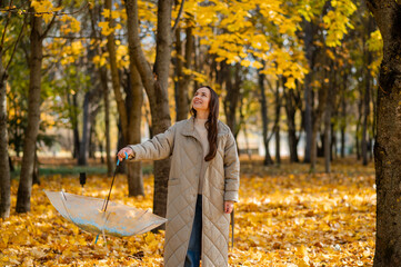 Conceptual portrait of woman in autumn park lifting umbrella with falling yellow maple leaves