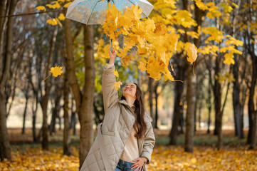Conceptual portrait of woman in autumn park lifting umbrella with falling yellow maple leaves