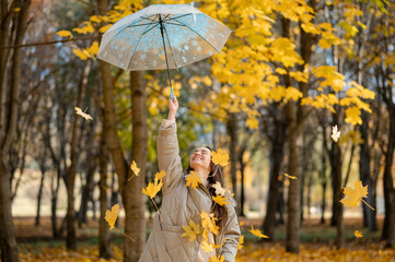 Conceptual portrait of woman in autumn park lifting umbrella with falling yellow maple leaves